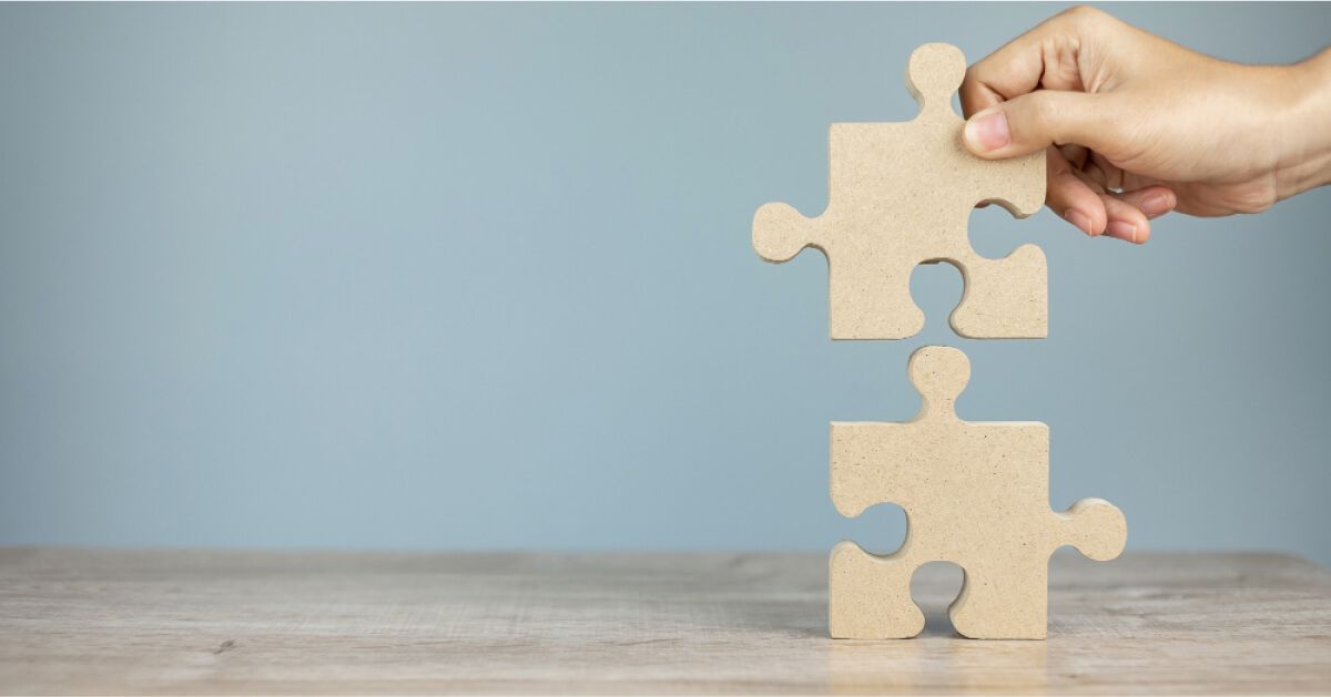 A hand putting together two oversized wooden puzzle pieces