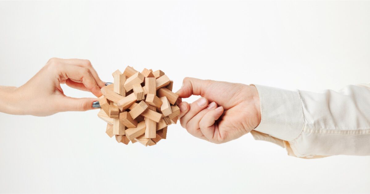 Two people holding onto a ball composed of interlinked wooden blocks