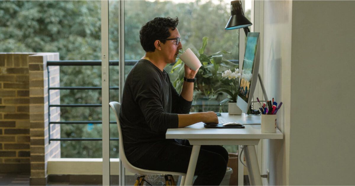 Person sipping a drink in front of a desktop screen